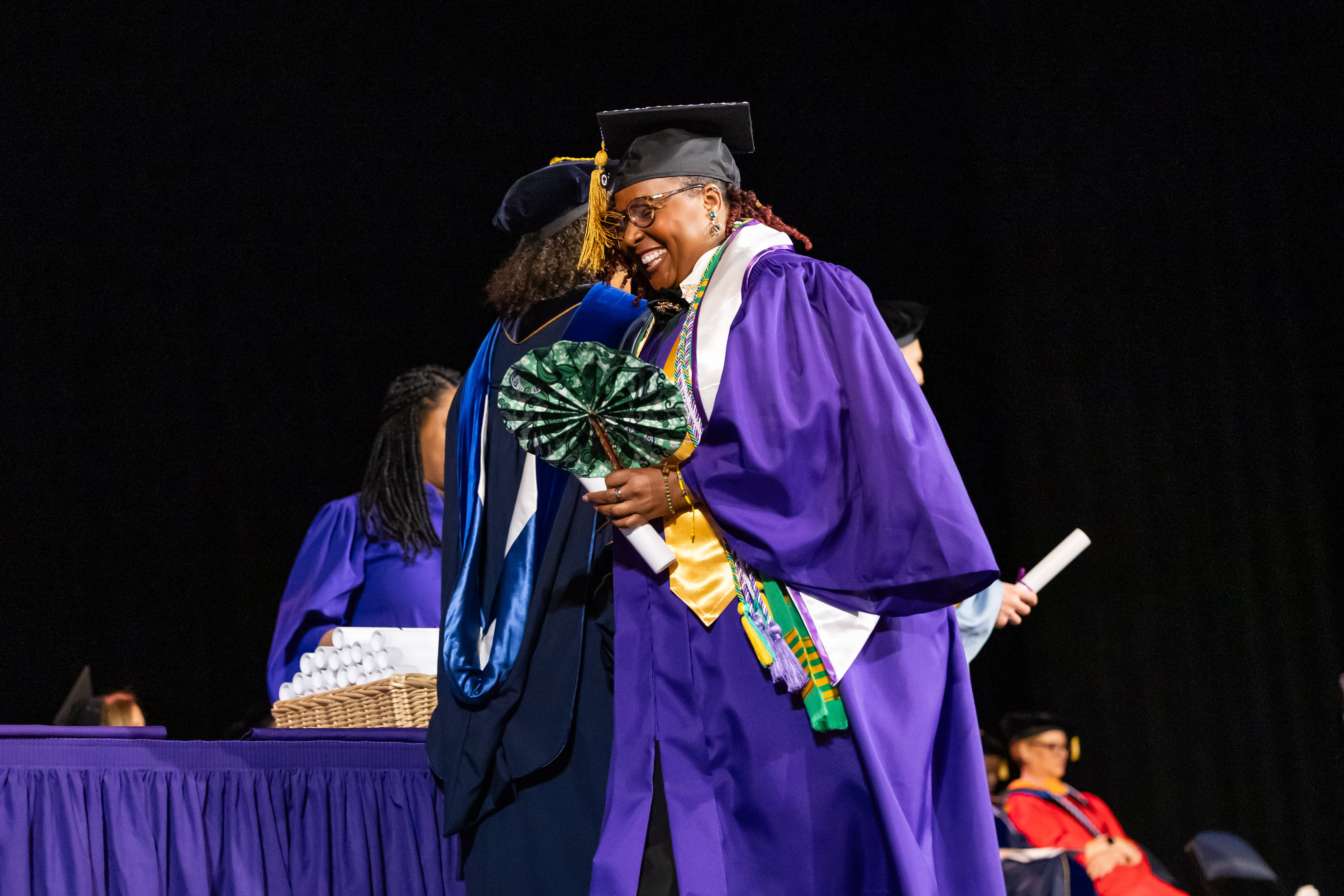Jasmin LeCadre on graduation stage hugging professor, smiling